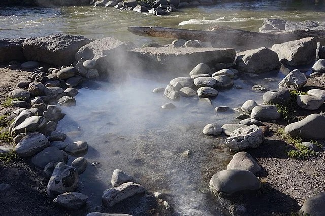 Steam rising from a natural hot-water spring among river rocks